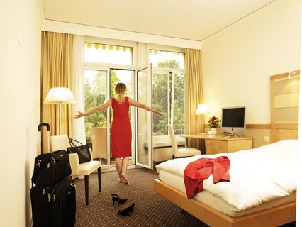 Frau öffnet Balkontür im Doppelzimmer im Park-Hotel am Rhein
